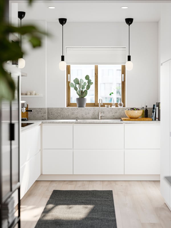 A small kitchen with white walls and smooth white VOXTORP fronts has three black pendant lamps and a gray rug on the floor.