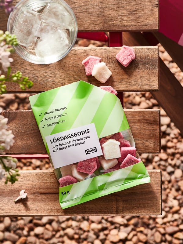 A packet of LÖRDAGSGODIS sour foam candy on the wooden slats of a table, pieces of candy are on the wooden slats.