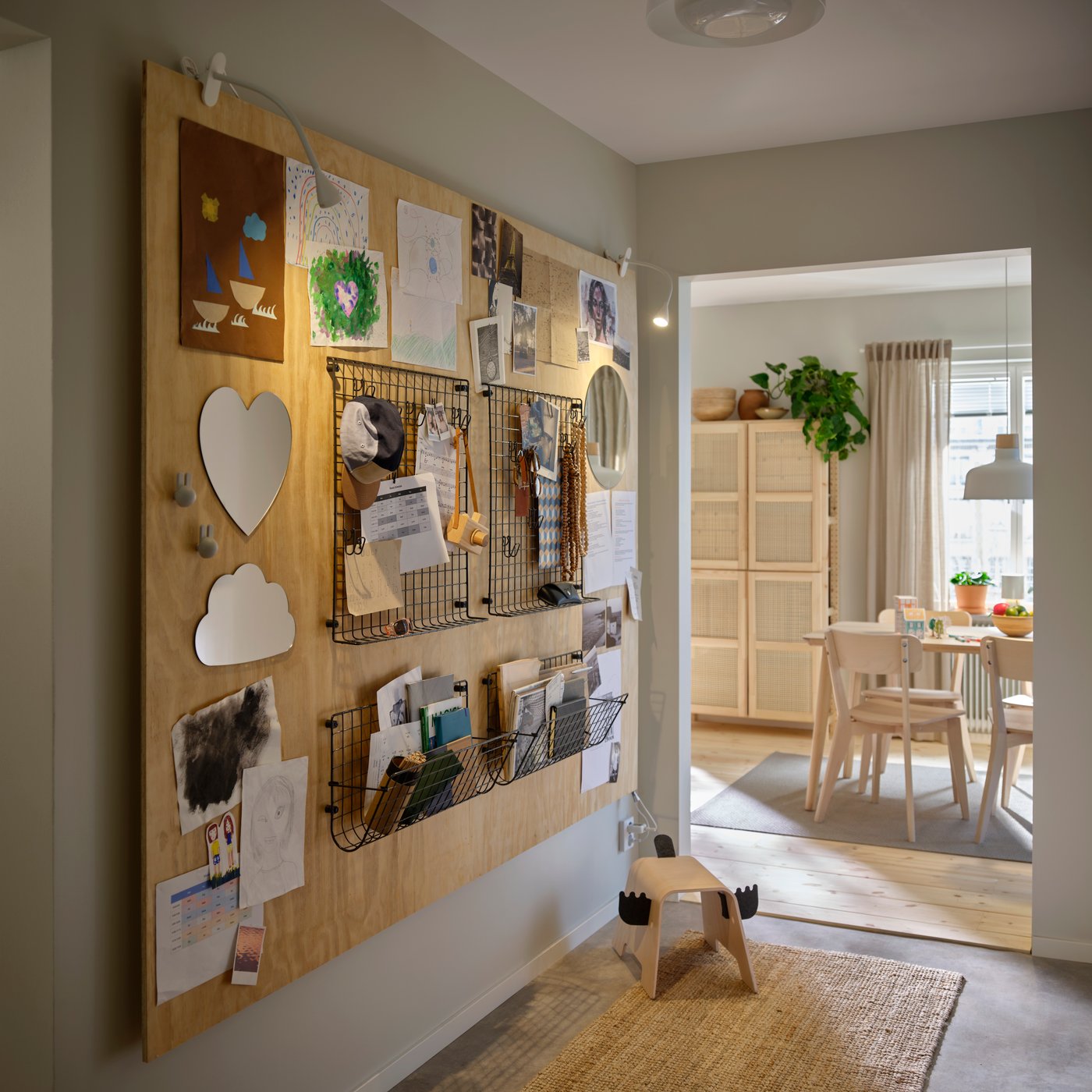 Un mur de couloir équipé de la poche murale GREJJIG utilisée pour ranger les papiers et les petits objets à côté des crochets et des planches.