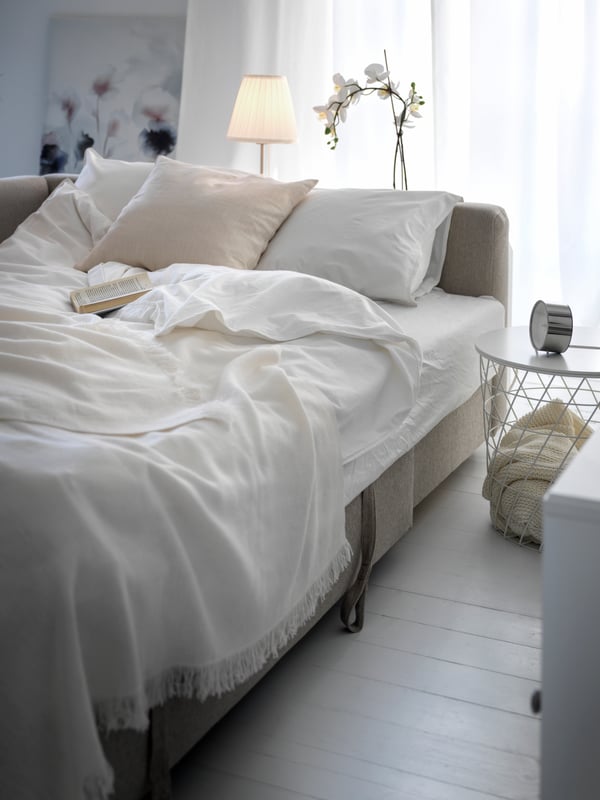 An unfolded beige FRIHETEN sofa bed with white bedding.