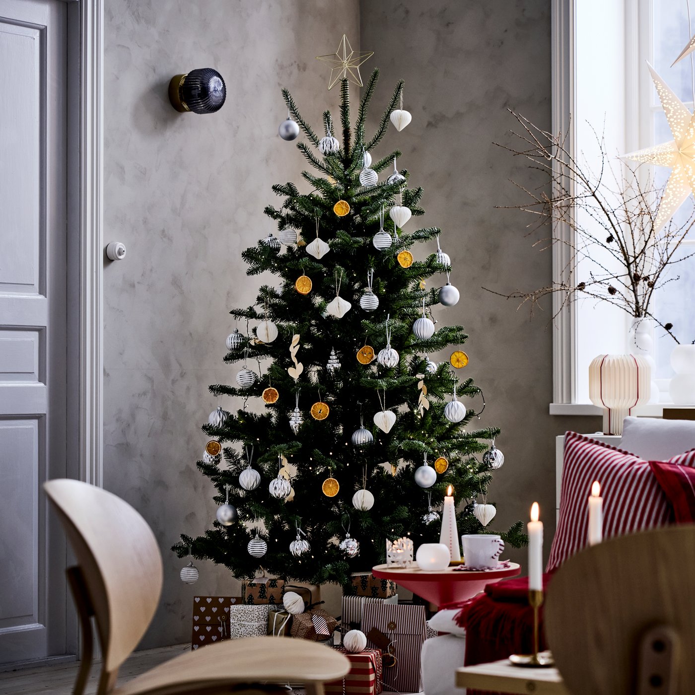 In een hoek van de kamer, naast een raam, staat een kerstboom versierd met zilveren en gouden VINTERFINT-kerstboomversieringen.