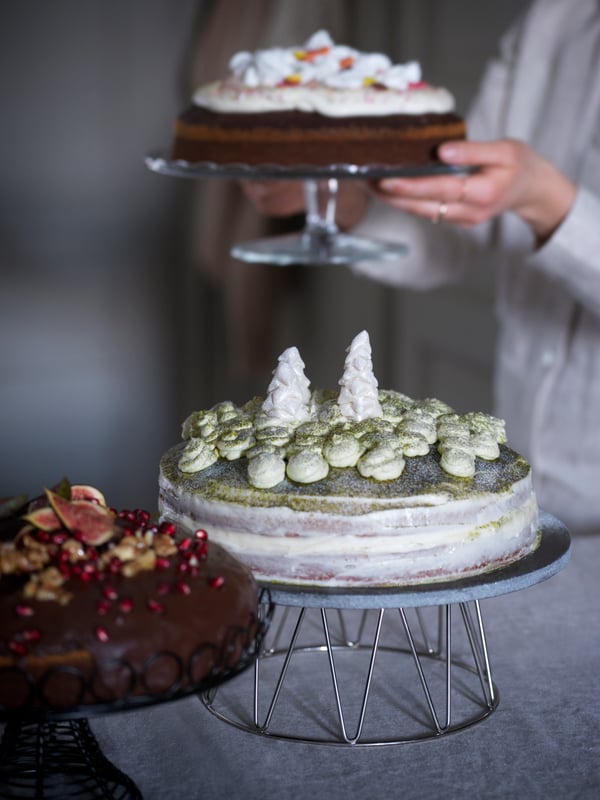 Eine Torte mit Winterwalddekoration ist hier auf einem BAKGLAD Kuchenteller zu sehen. Im Hintergrund hält jemand eine weitere Torte in den Händen.