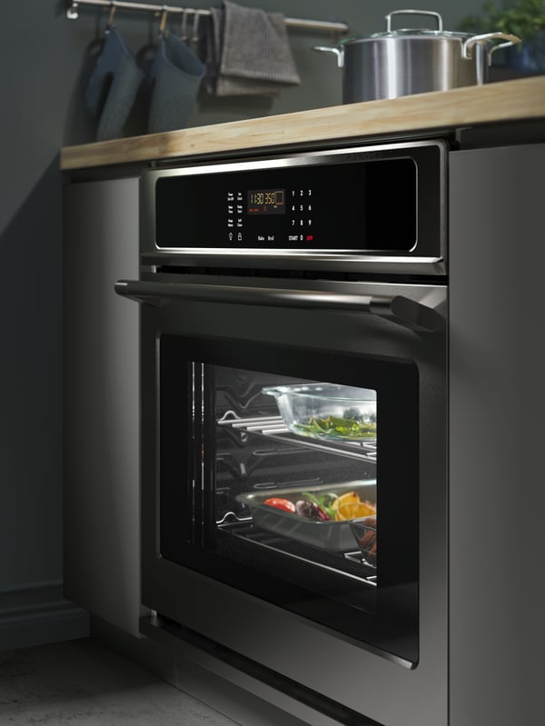Horno mural KONSISTENS de acero inoxidable en una cocina con frentes VOXTORP de color gris oscuro, barra de fresno/vena y un riel con ganchos.