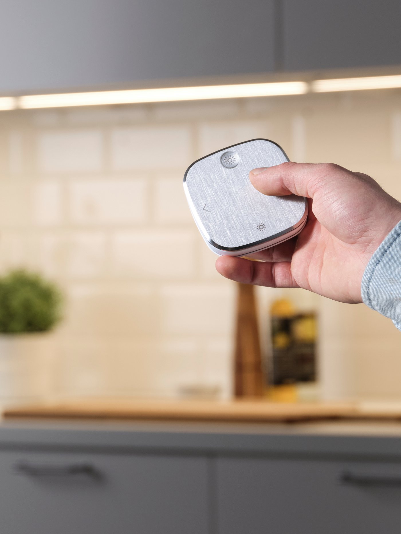Hand holding a STYRBAR remote with a kitchen in the background