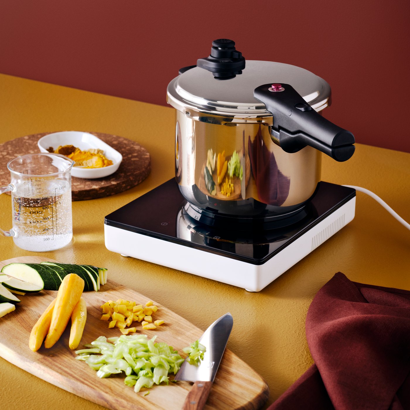 Autocuiseur IKEA 365+ en acier inoxydable sur une table de cuisson à induction mobile TILLREDA blanche, planche à découper et couteau.