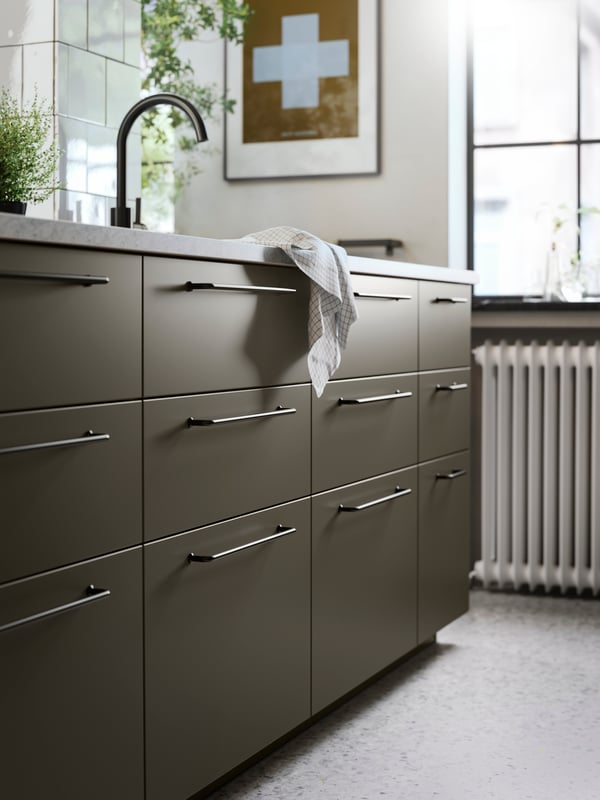 En køkkenø med brun-beige HAVSTORP køkkenfronter, sorte greb, et køkkenbord med kalkstensmønster og en sort vandhane.