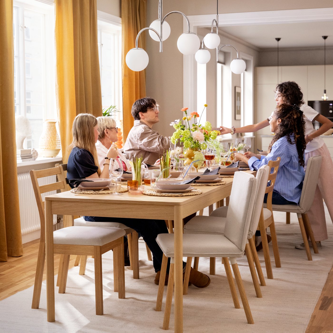 A family sitting around a TONSTAD table in oak veneer and a number of TONSTAD chairs, the table set for a festive occasion.