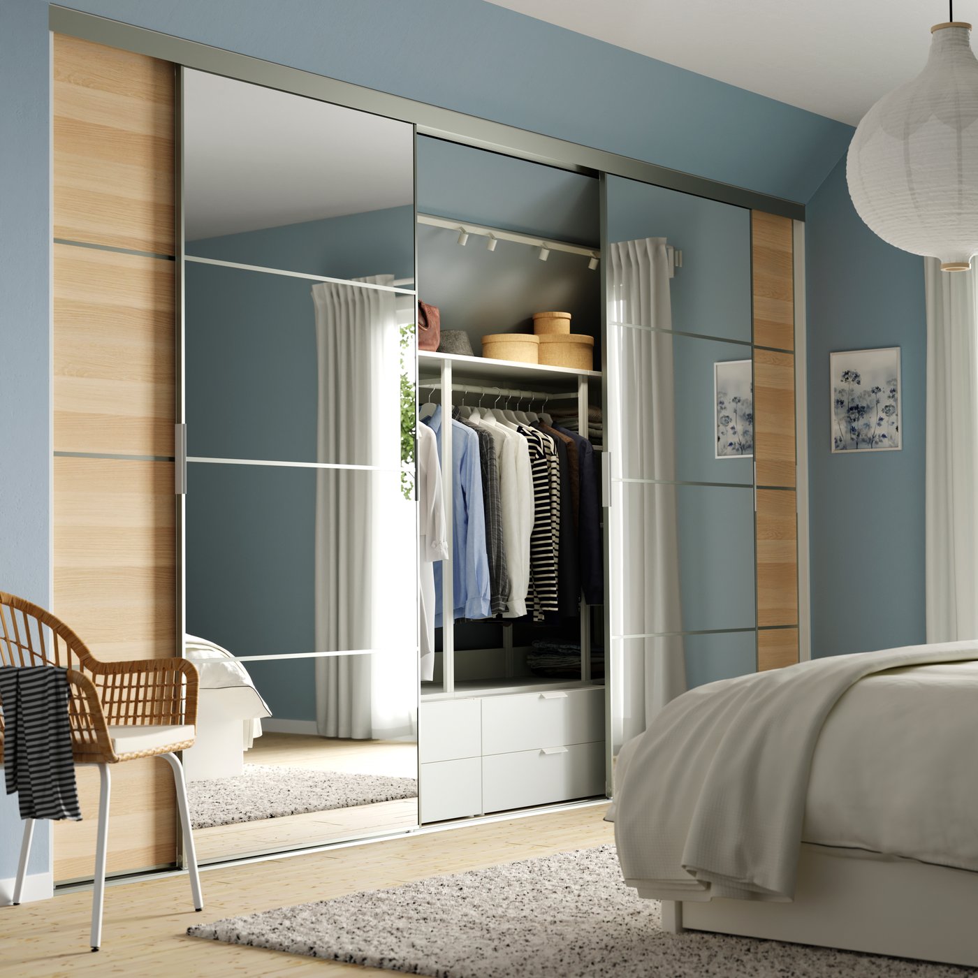 A SKYTTA sliding door solution in a bright bedroom. The doors are partly open, showing clothes and storage behind.
