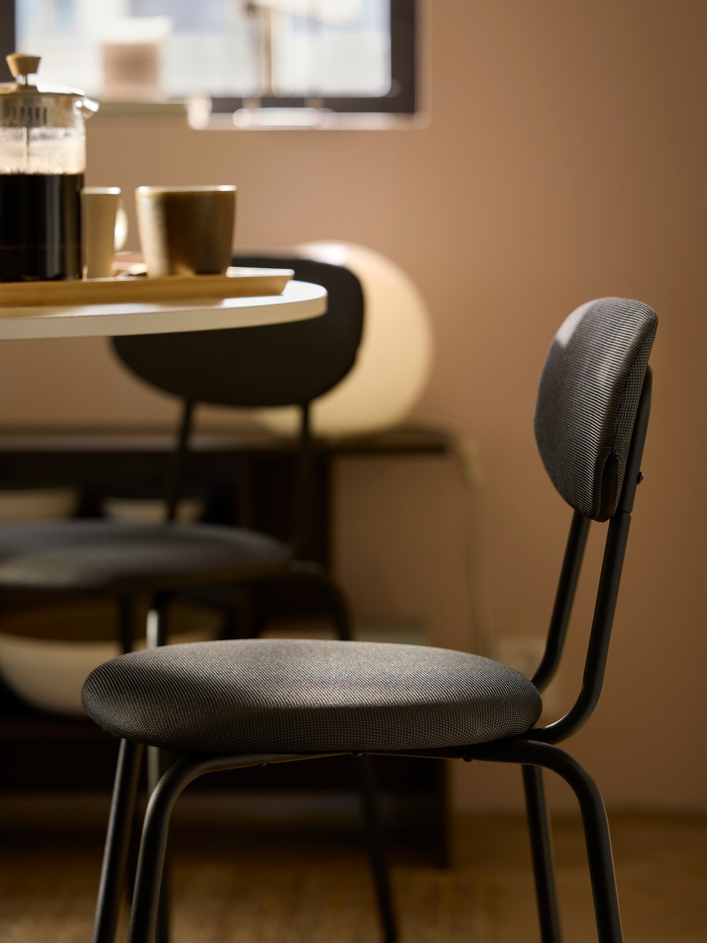 Black ÖSTANÖ chairs standing in a sun-dappled dining area next to a white, round DOCKSTA table with coffee accessories on it.