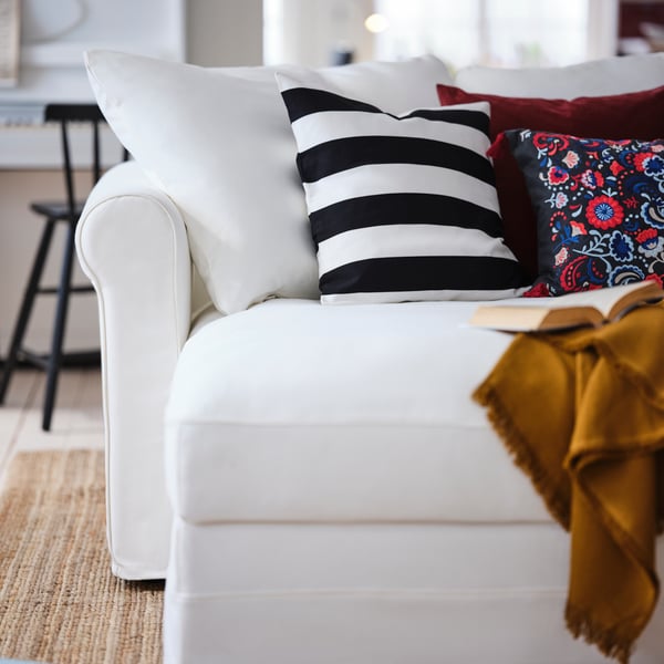 A living room where various colourful cushions and a throw occupy the chaise-longue part of a white GRÖNLID 4-seat sofa.