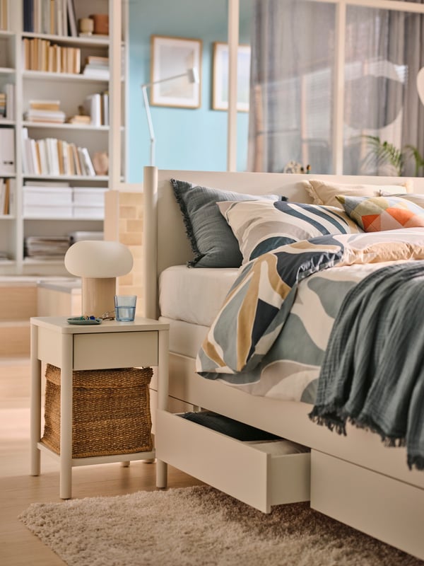 Ein weißes TONSTAD Bett steht in einem großen Schlafzimmer, darauf liegen bunte Kissen und Bettwäsche