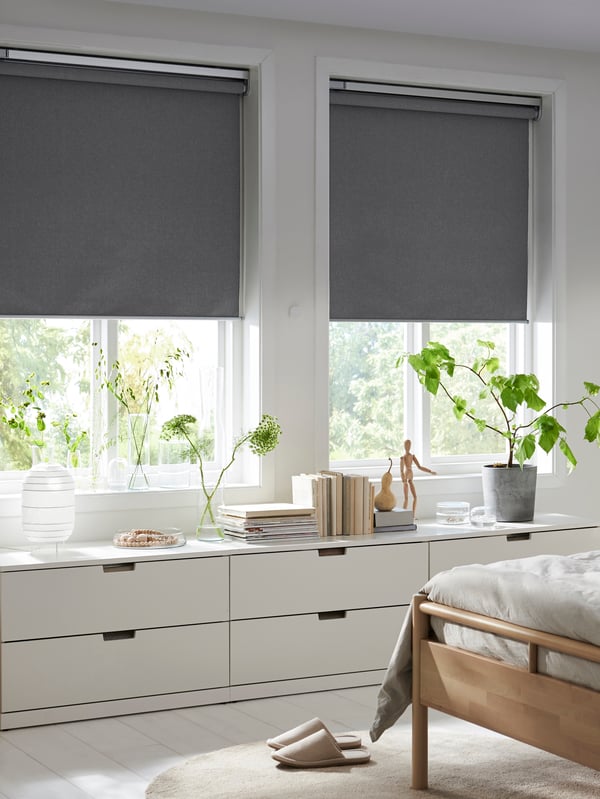 A bedroom with two FYRTUR block-out roller blinds, half-way down, in two windows above three low chests of drawers.