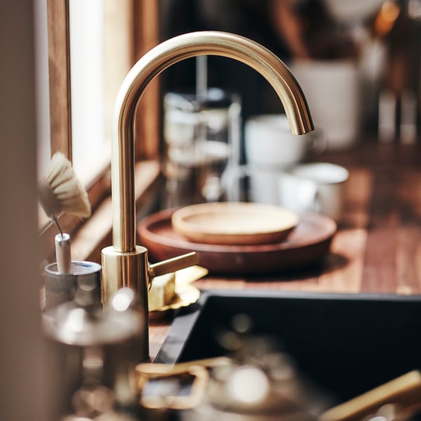 A close-up of a DELSJÖN kitchen tap above a sink with dishes and cups in the background.