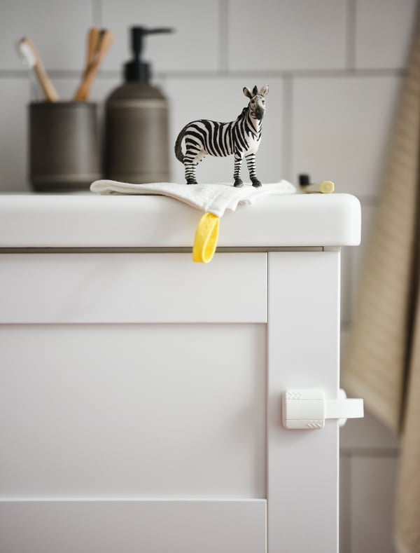 A close-up shot of a safety clip on a white vanity that is holding bathroom accessories and small toy giraffe.