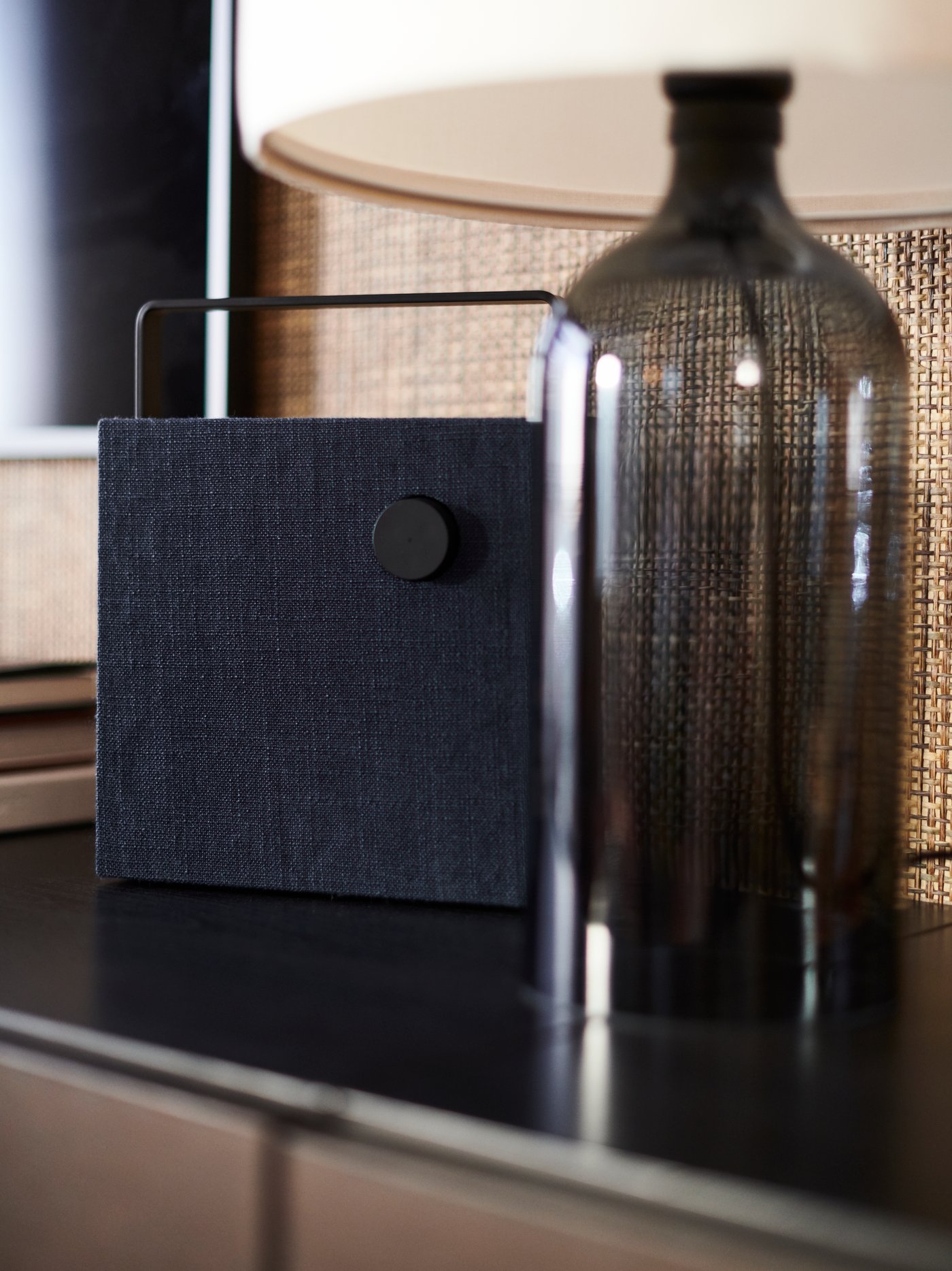 A TONVIS table lamp with a smoked glass base and white shade on a dark surface beside an ENEBY bluetooth speaker.