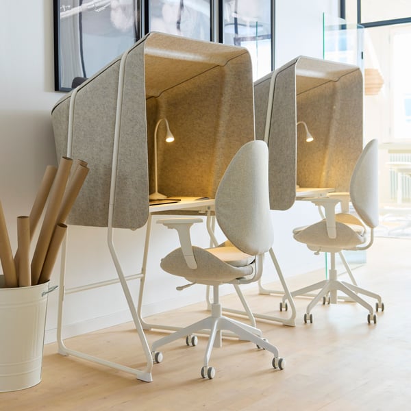 Une chaise de bureau HATTEFJÄLL GUNNARED beige-blanc devant un bureau avec un panneau acoustique dans un espace de travail.