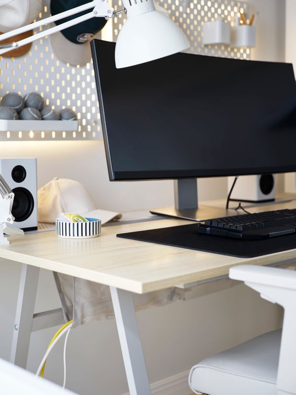 The ash effect top and grey legs of an UTESPELARE gaming desk seen from a corner. Cables hang in the attached net bag below.