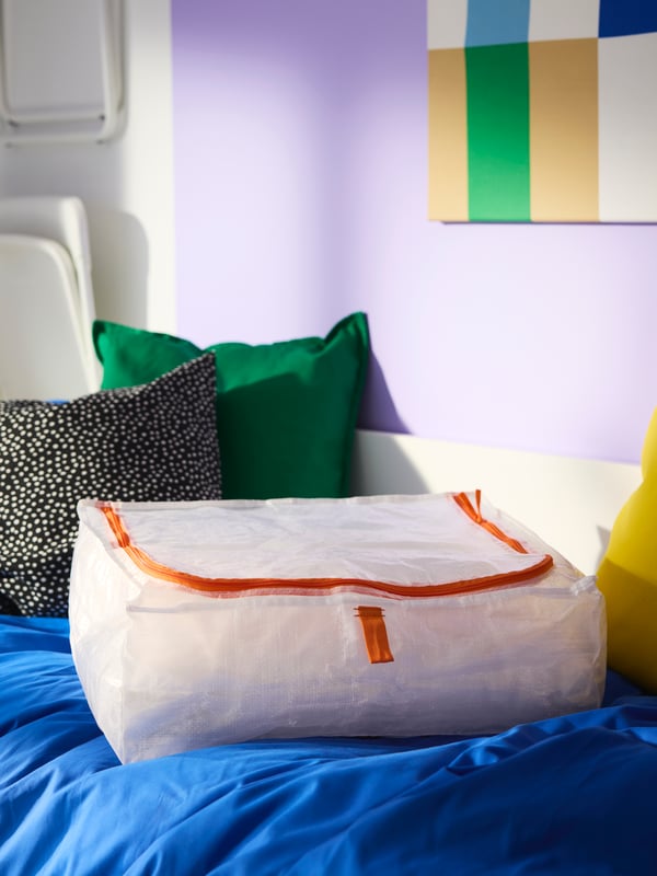 PÄRKLA storage case with orange details, on top of bed with duvet cover and cushions in different bright colours.