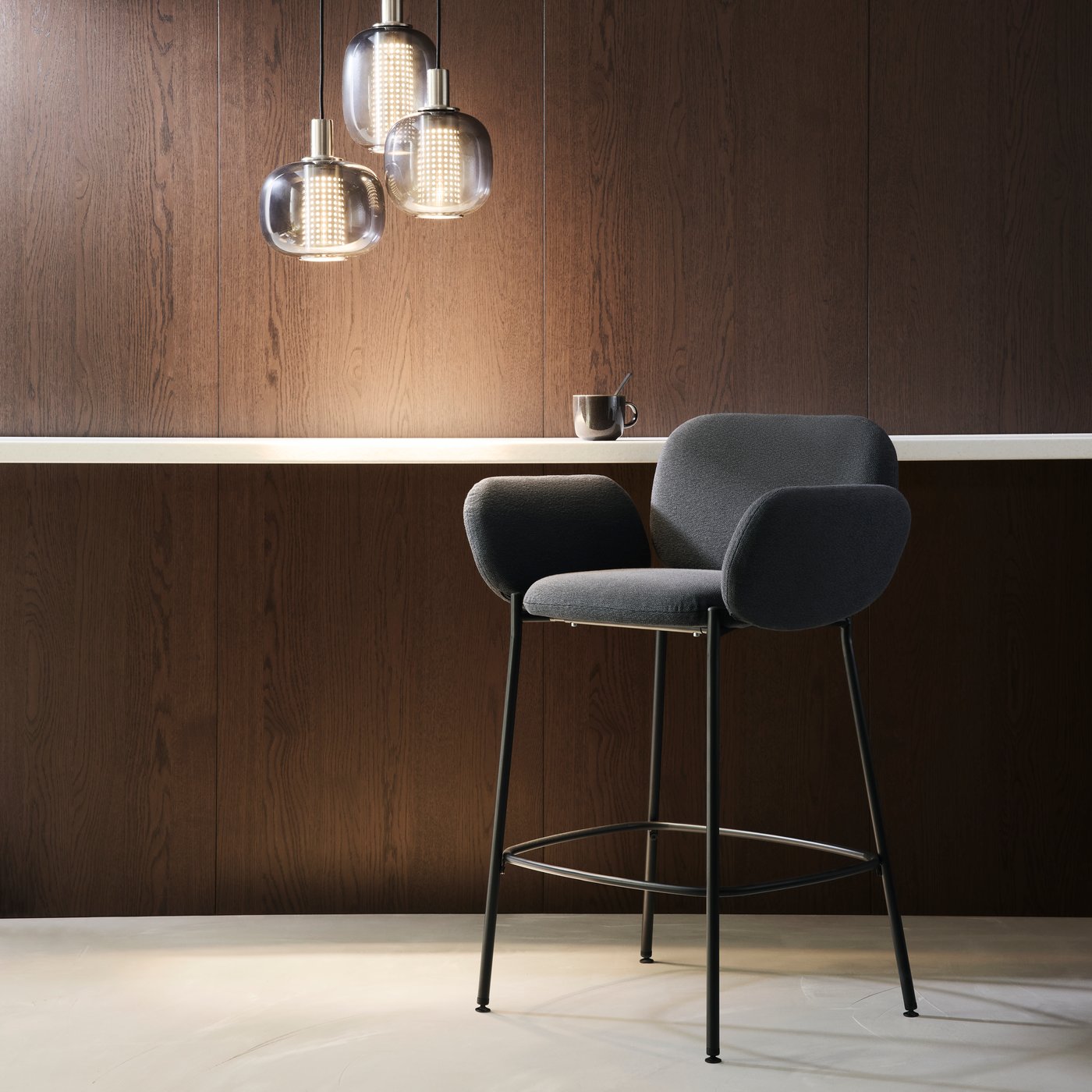 En sort/antracitfarvet SYNTORP barstol med ryglæn står i et rum med en HÖGVIND loftlampe med 3 lamper.