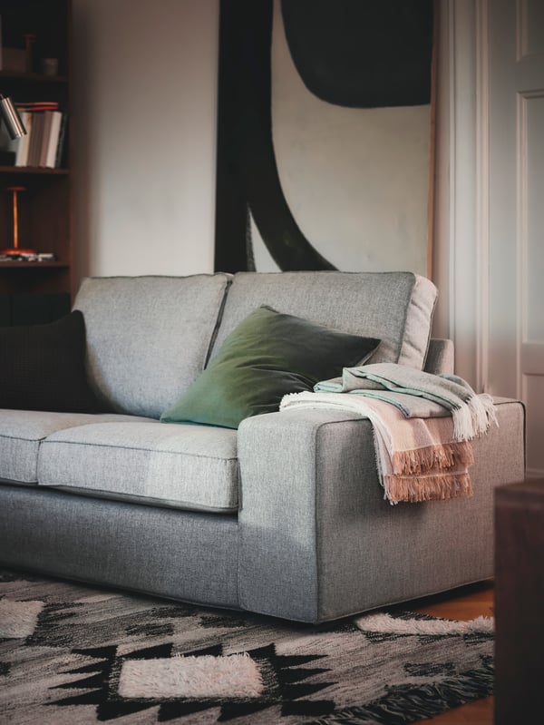 A KIVIK 2-seat sofa with cushions and throws stands in a corner of a living room with the front part on a flatwoven rug.