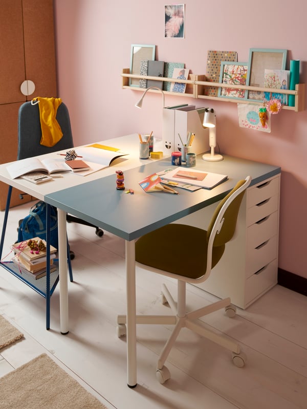 Two desks in white and blue with swivel chairs placed together facing each other in a children’s room in pastel tones.