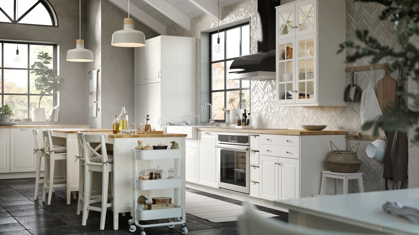 A SEKTION kitchen with BODBYN doors and glass doors in off-white, a RÅSKOG cart, BUNKEFLO pendant lamps in beige/birch.