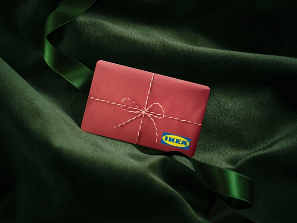 Crvena IKEA poklon-kartica sa slikom ukrasne mašnice i IKEA logotipom na zelenoj somotskoj tkanini.