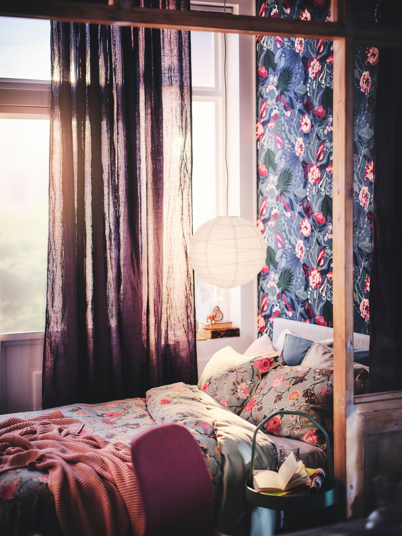 A bed with a throw and bed linen dressed in a NÄSSELKLOCKA duvet cover and pillowcase set, with a pendant lampshade above.