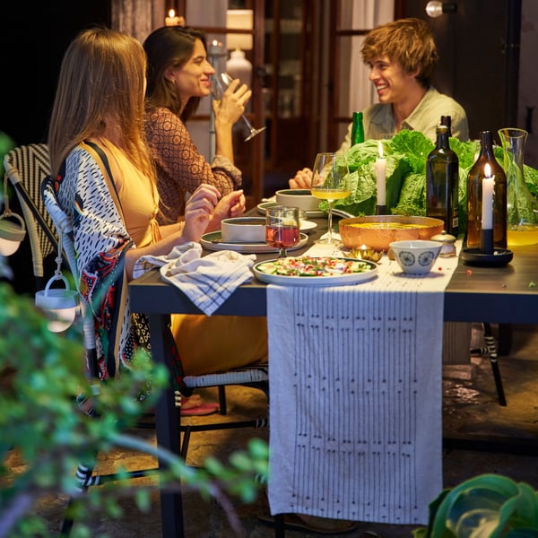 Tre personer sitter på en uteplats och njuter av en god middag tillsammans.