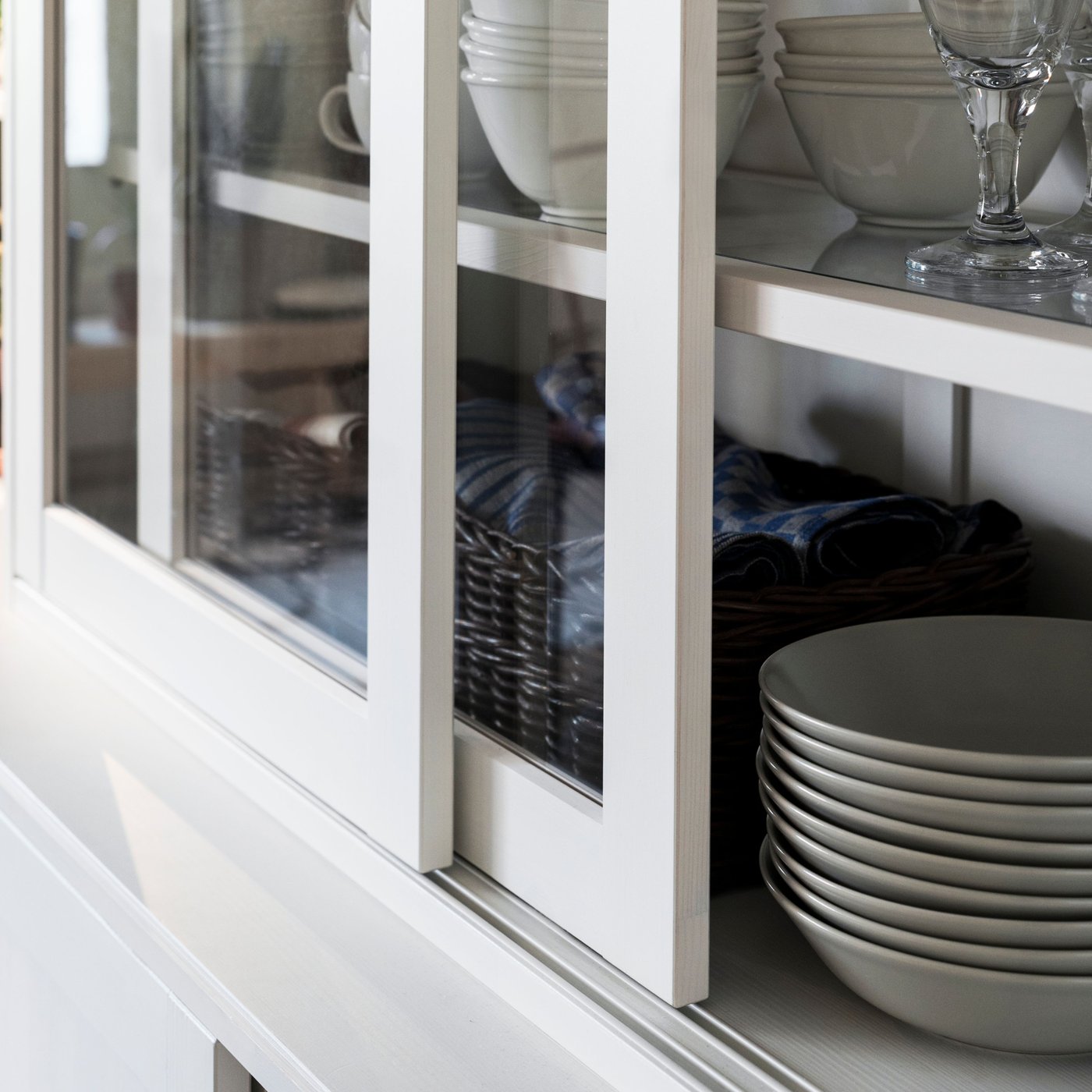 Bowls, glasses and other tableware stand on shelves inside a white HAVSTA glass-door cabinet with open doors.