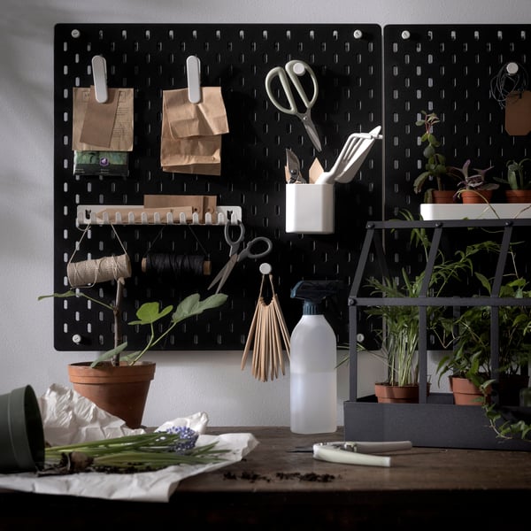 Miscellaneous gardening accessories arranged on black SKÅDIS pegboards, wall-mounted over a worktop with potted plants.