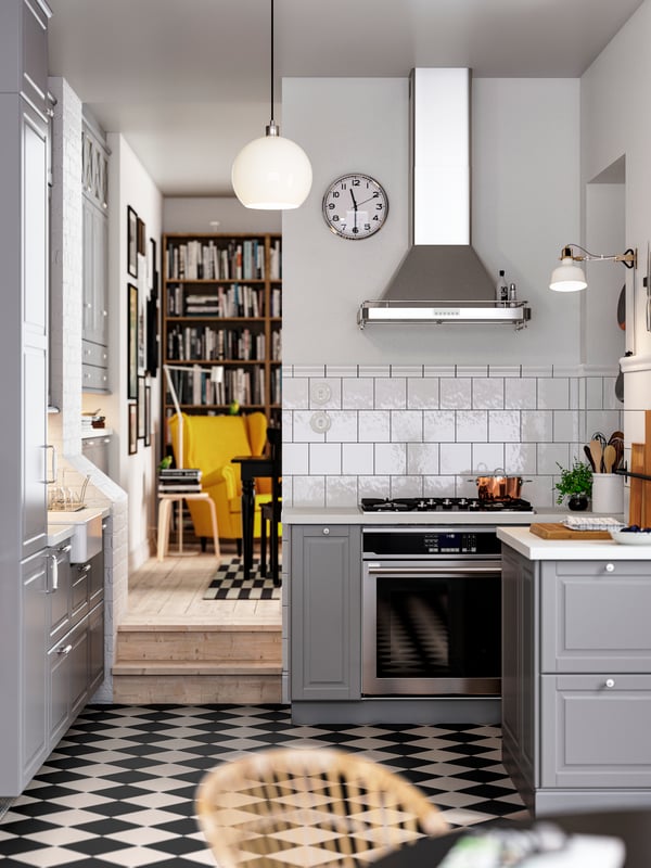 A kitchen with a chequered floor, grey BODBYN fronts with off-white/chrome plated handles and knobs, plus a pendant lamp.