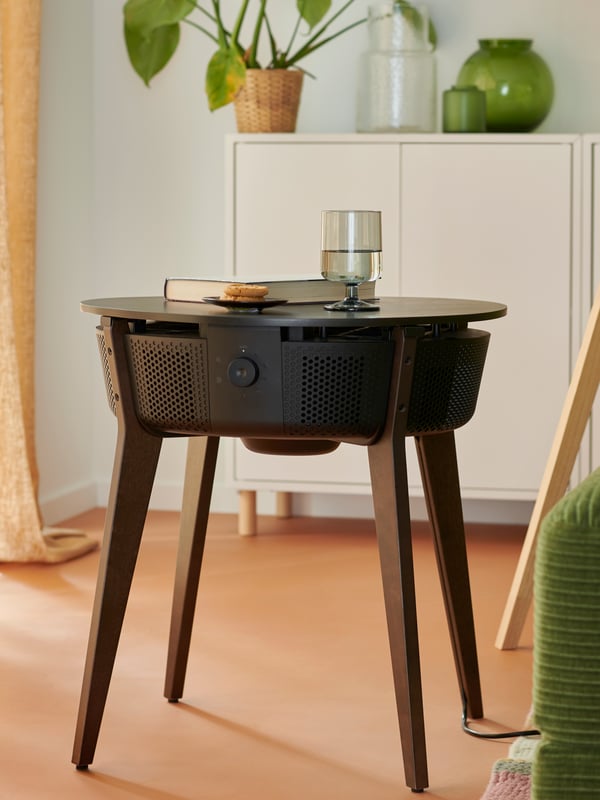 A STARKVIND table with air purifier in a living room with a glass of water, a small plate of cookies and a book on top.