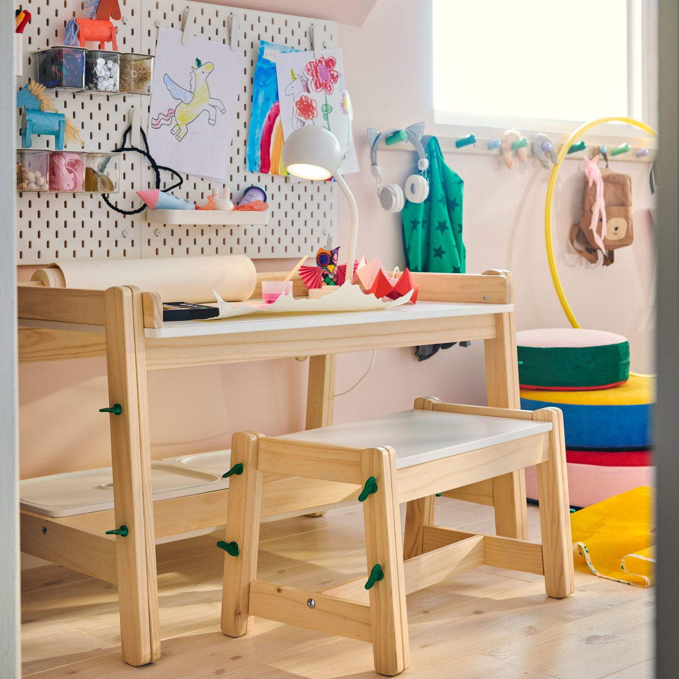 A FLISAT desk with storage boxes in pine, with a matching bench, in a children’s room beside a pegboard wall with artwork.