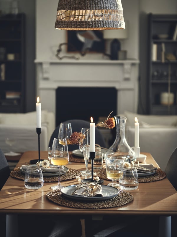 An extended DANDERYD drop-leaf table festively set with IHÅLLIG seagrass place mats, DYRGRIP wine glasses and decorations.