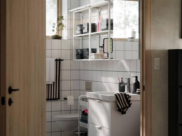 A bright and modern bathroom with white HAVBÄCK/ÖRRESJÖN storage, white open ENHET shelves on the wall and  striped towels.