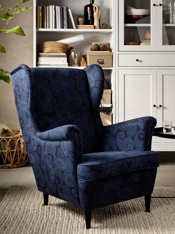 A dark blue wing chair, a white bookcase, books, dark beige storage boxes with lids, decorative objects.
