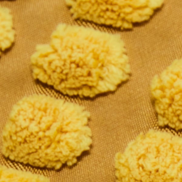 A close-up of the pom-pom detail of a yellow SVARTPOPPEL cushion cover.