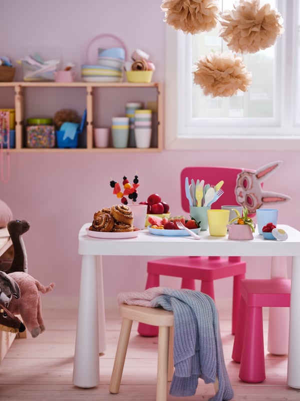Una mesa con peluches y en frente una silla MAMMUT rosada. 