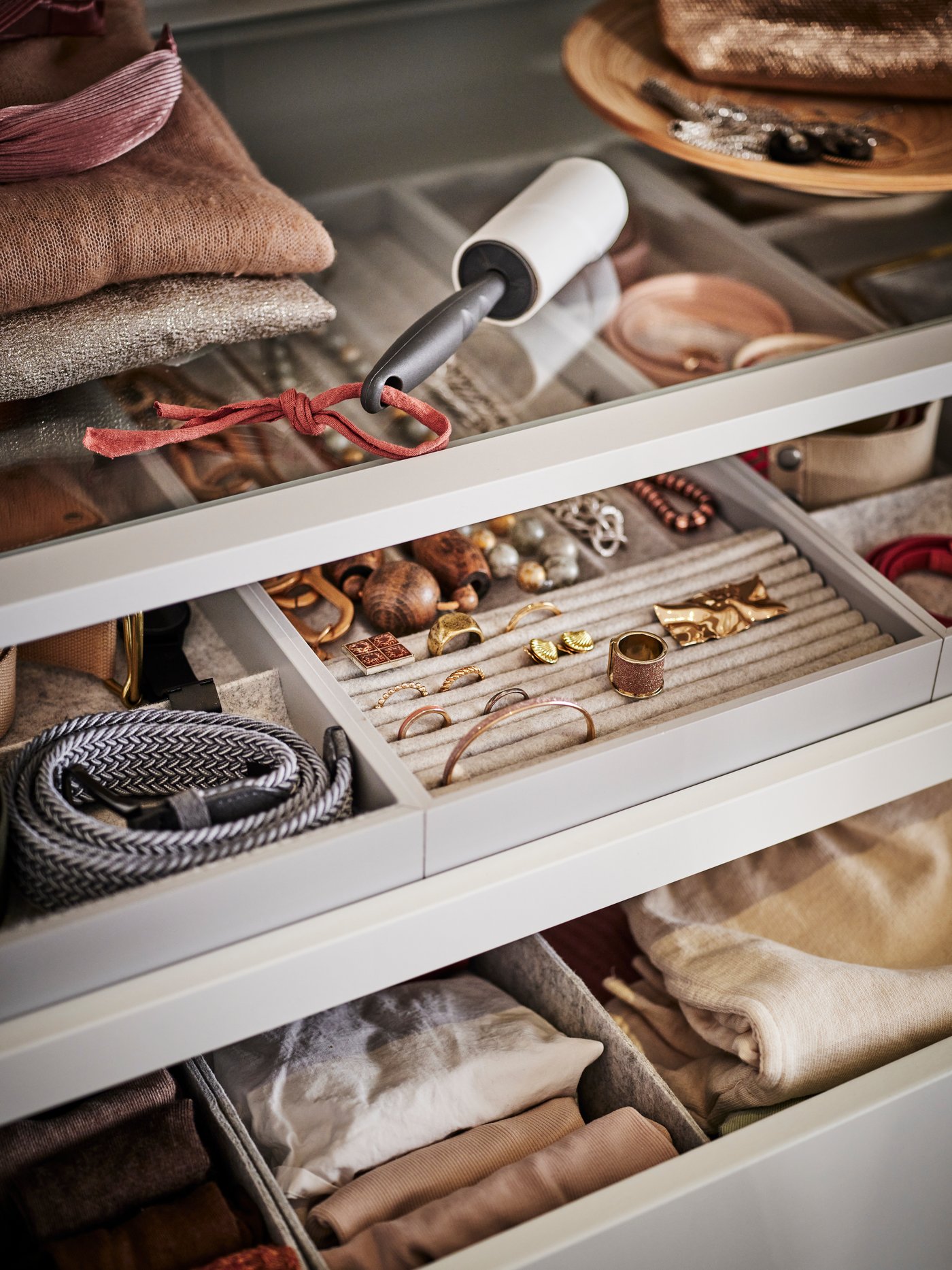 Zwei KOMPLEMENT-Ausziehfächer mit Einsätzen in einem Kleiderschrank, in denen verschiedene Accessoires wie Schmuck, Gürtel und eine Fusselrolle aufbewahrt werden.