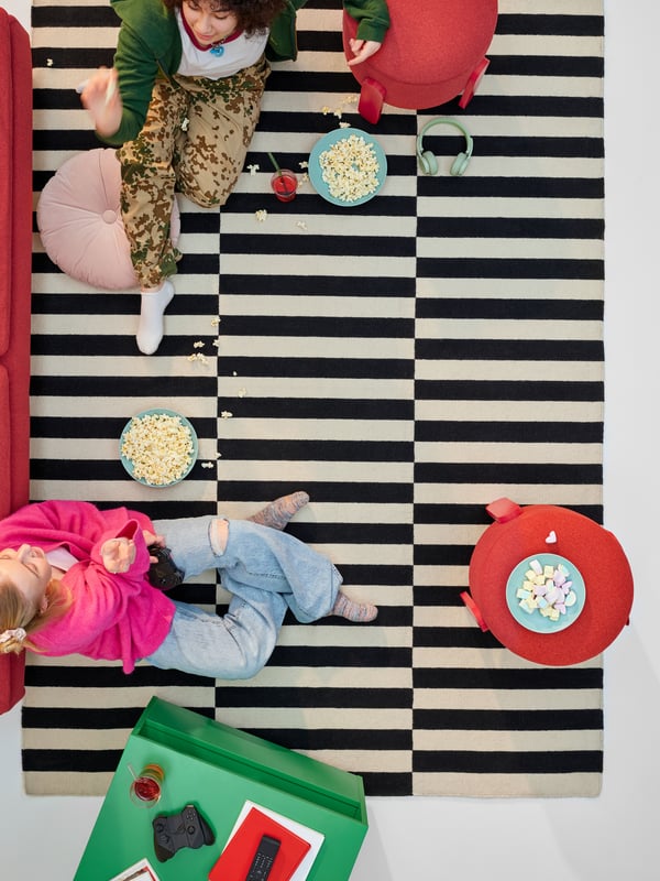 A bird's eye view of an IKEA STOCKHOLM rug in black and beige stripes with two people lounging on top.