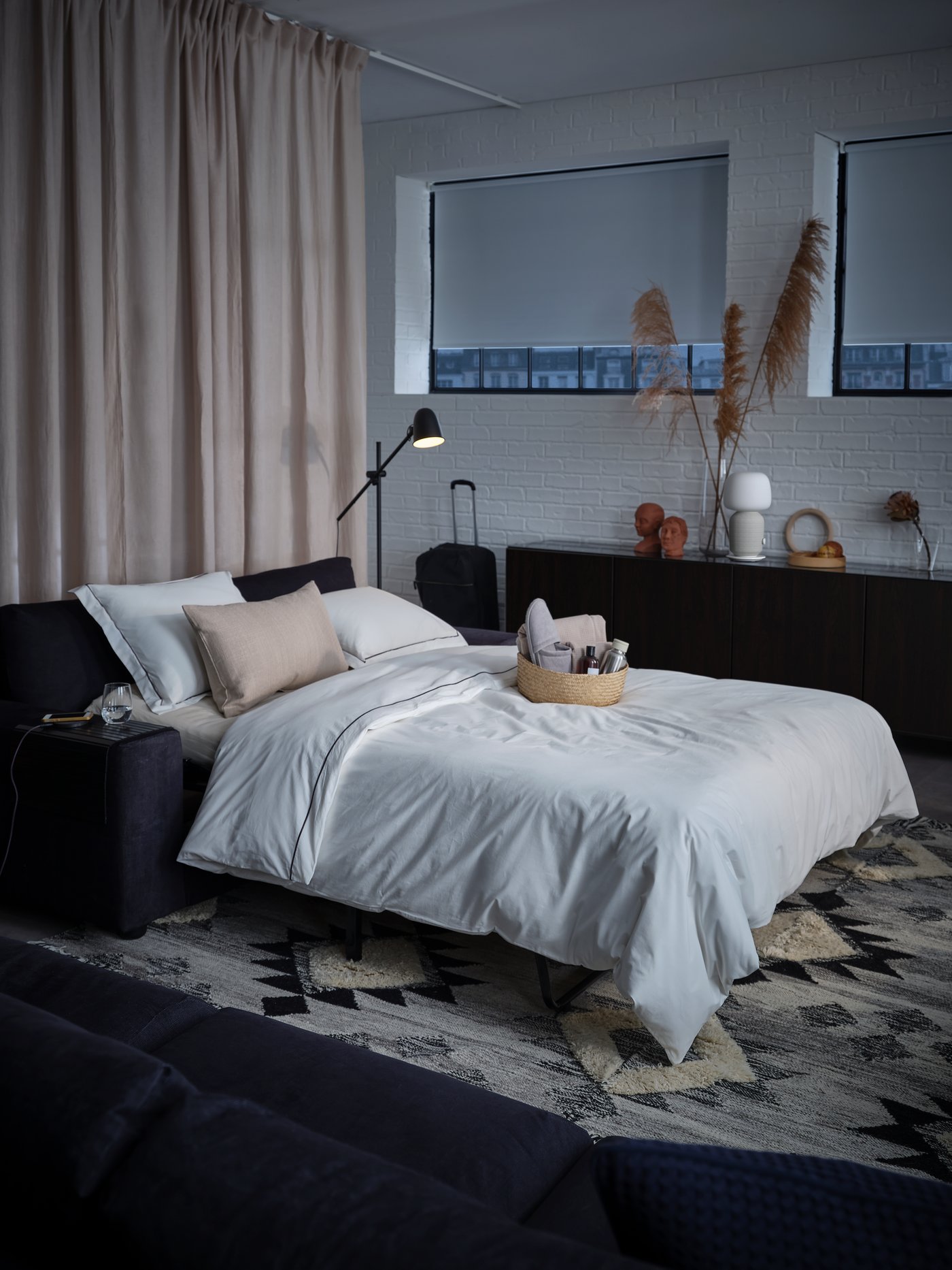 Ruang dengan sofa katil dua tempat duduk VIMLE mod katil, langsir DYTÅG berwarna kuning air dan bakul yang menarik dengan kelengkapan dandanan diri di atas katil.
