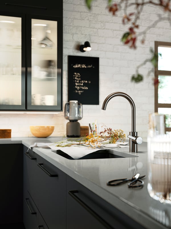 Una cocina con fregadero KILSVIKEN, frentes de cajón NICKEBO en carbón mate, una lámpara con altavoz SYMFONISK sombreada de vidrio con Wi-Fi.