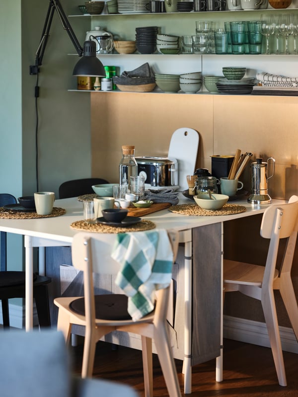 Four chairs around a KALLHÄLL gateleg table with storage set for breakfast, with crockery on the shelves above.