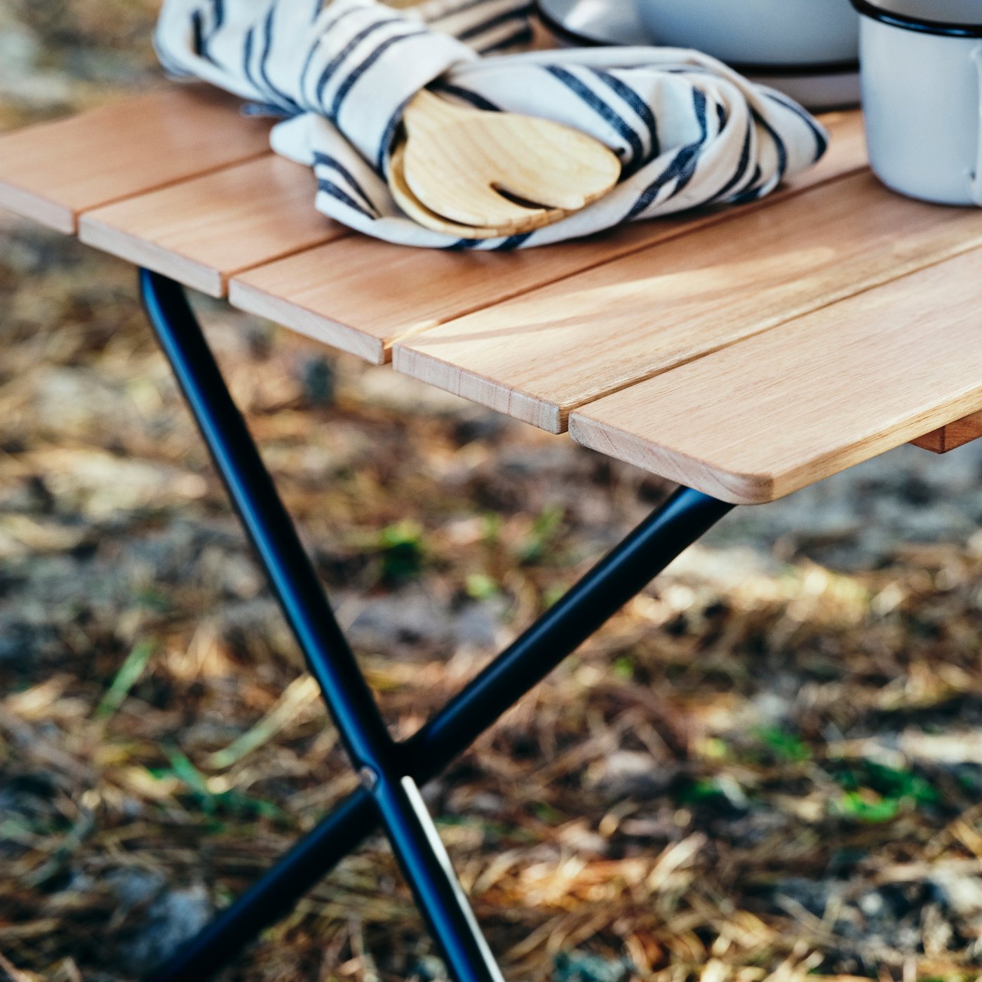 The SOLUPPGÅNG folding table is standing outdoors, with a SOLUPPGÅNG 2-piece salad server set and tea towel on top.