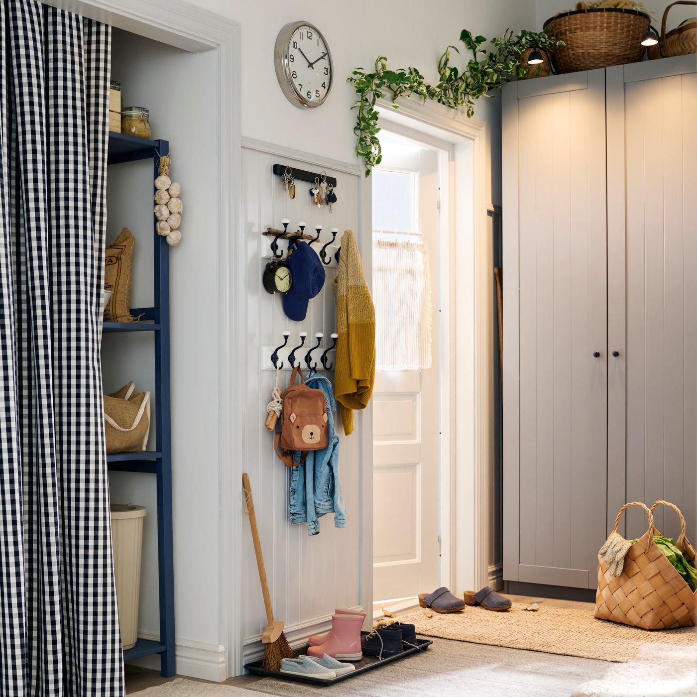 The corner of a large hallway with a door and a wardrobe in the back, a pantry behind a curtain and hooks on the wall.