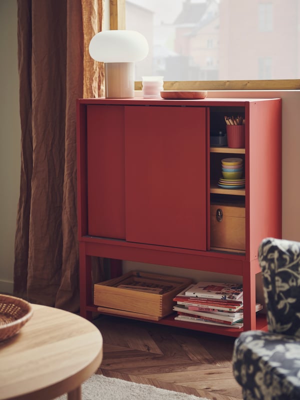 An IVAR cabinet with sliding doors – painted in red – contains children’s toys and art materials in a living room.