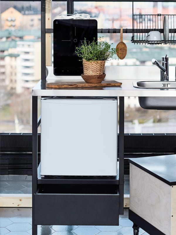 A TILLREDA mini kitchen, a green plant in a plant pot on a chopping board and a coffee-table/side-table on castors.