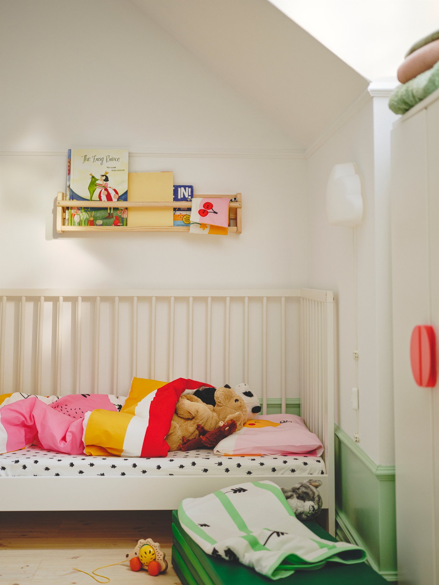 Een GULLIVER ledikant opgemaakt met meerkleurig/gestreept GRÖNFINK beddengoed met ernaast een GRÖNFINK deken met groen/boommotief.