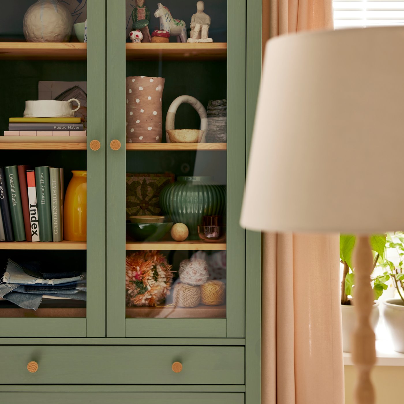 A KINNAHULT floor lamp stands in front of a window with LENDA curtains near a HEMNES glass-door cabinet with 3 drawers.